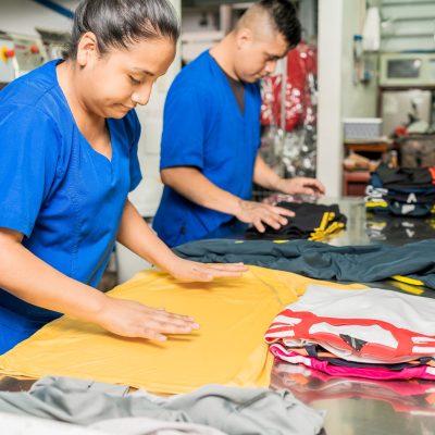 Latino,Employees,In,Uniform,Folding,Clothes,In,An,Industrial,Laundry